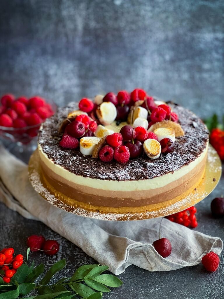 Delicious chocolate layered cake topped with fresh berries and meringue on a rustic backdrop.